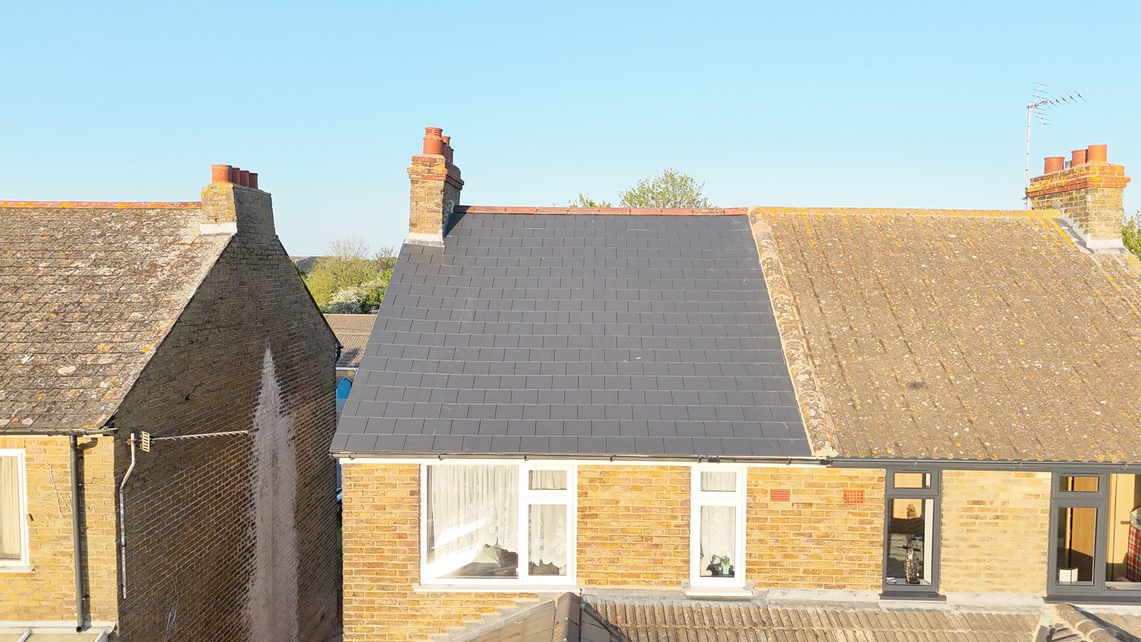 A finished slate re-roof by StoneRidge Roofing beside its neighbours' original weathered roofs